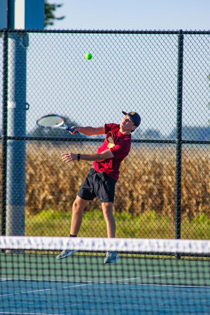 Senior doubles player John Kiesel launches a serve earlier in the season against Forest Park.