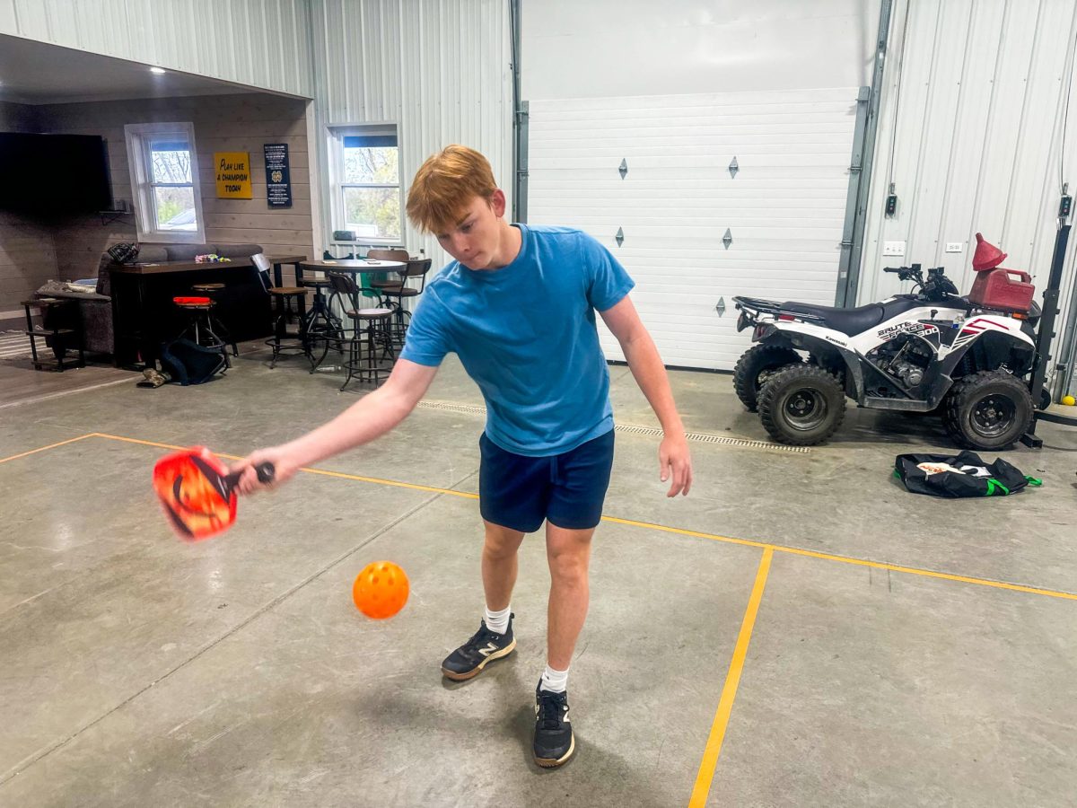 Sophomore Collin Higginbotham returns a serve in a friend's shed, where they have created a pickleball court. 