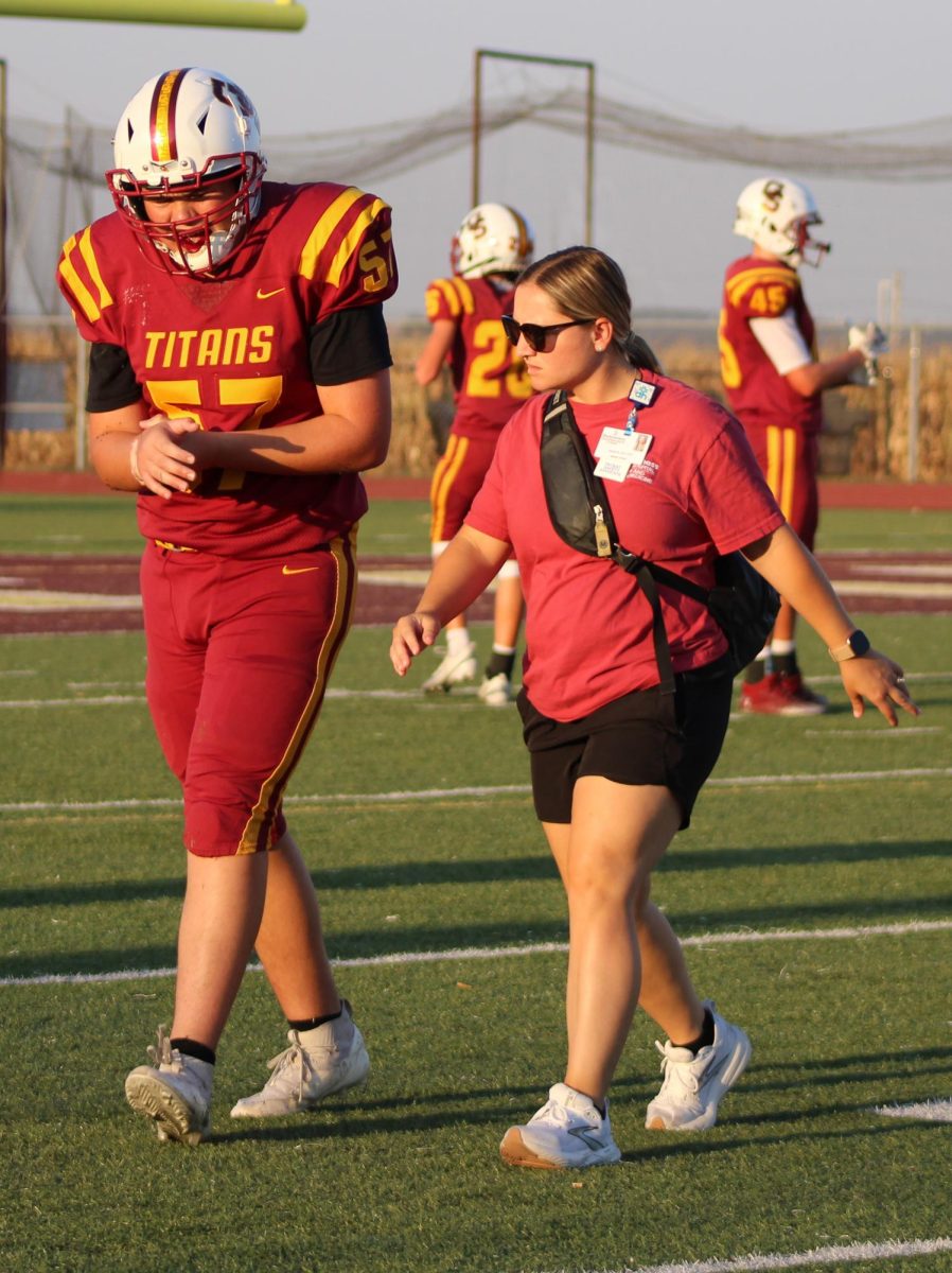Athletic trainer Jenna Sparks listens to junior Gavin McEllhiney before examining his wrist on the sideline.